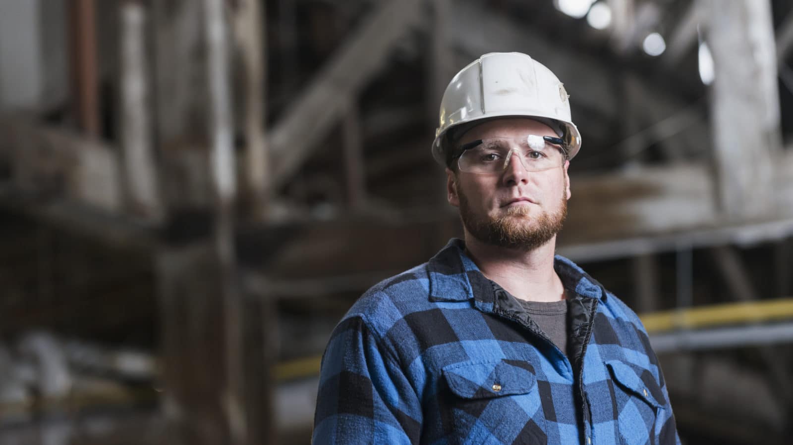 Man wearing hardhat, safety goggles and plaid shirt