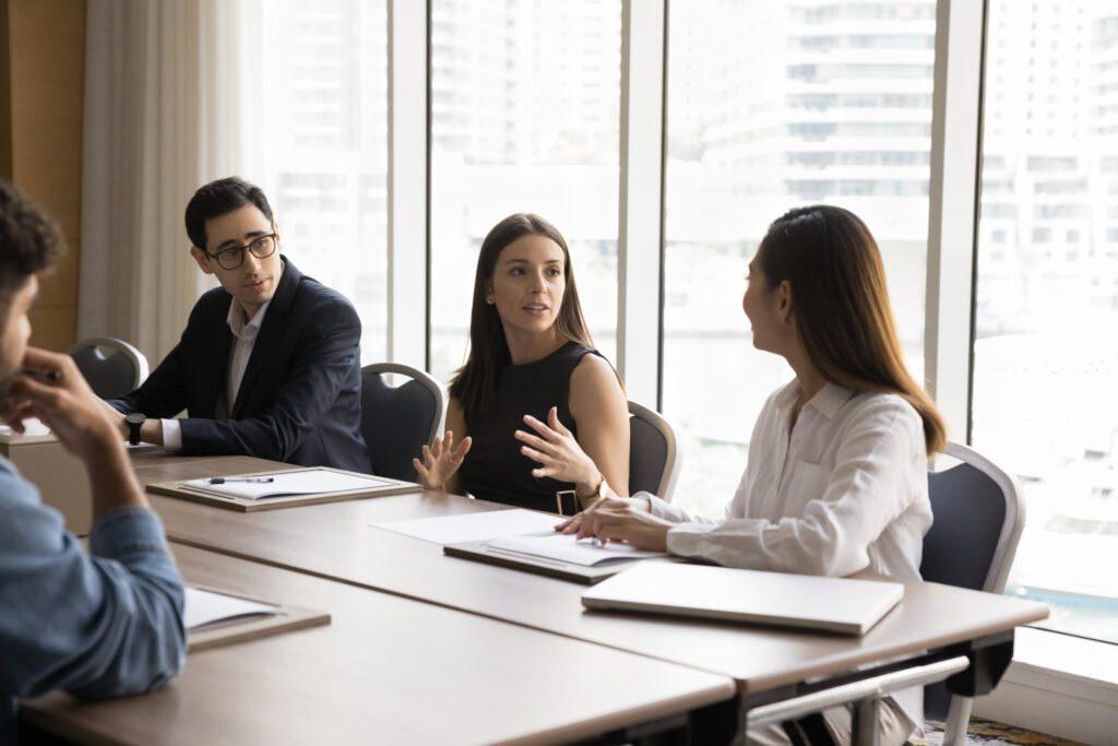 Inspired young business woman talking to colleagues on brainstorming meeting, discussing work strategy, project management, creative ideas. Corporate coach training employees class of 2024 law graduates