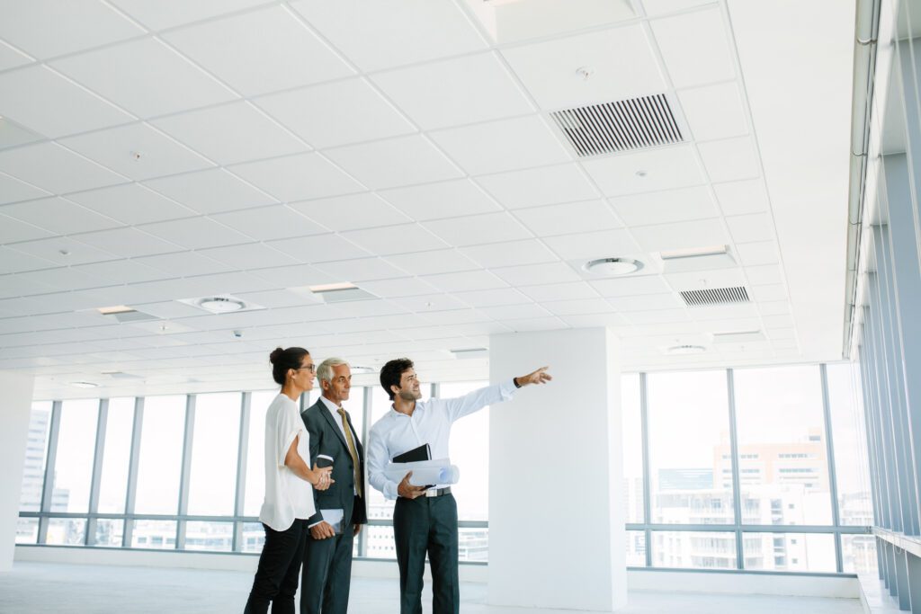 Real estate broker showing office space to clients. Business people and real estate agent at empty office space, with estate broker pointing at something interesting. law firm return to office