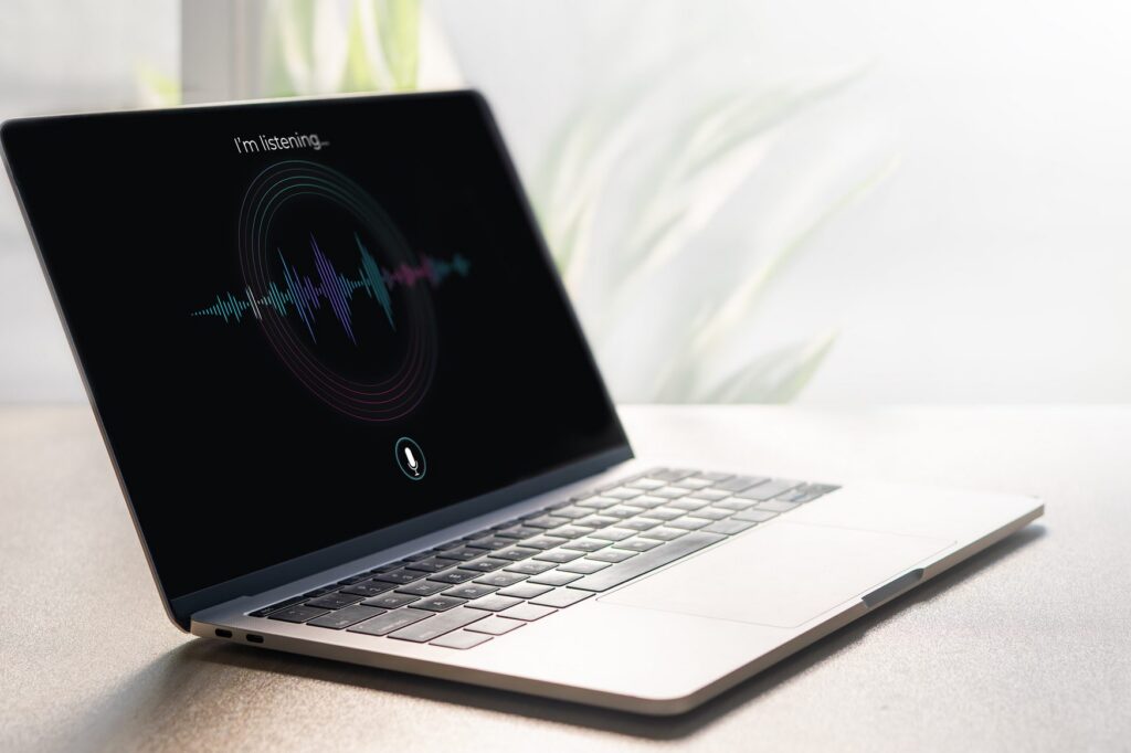 AI notetakers for lawyers; A laptop on a modern bright desk displays a dark screen showing an AI voice assistant interface with colorful sound wave visualization, circular rings, microphone icon, and the text I'm listening, representing voice AI and speech recognition technology.